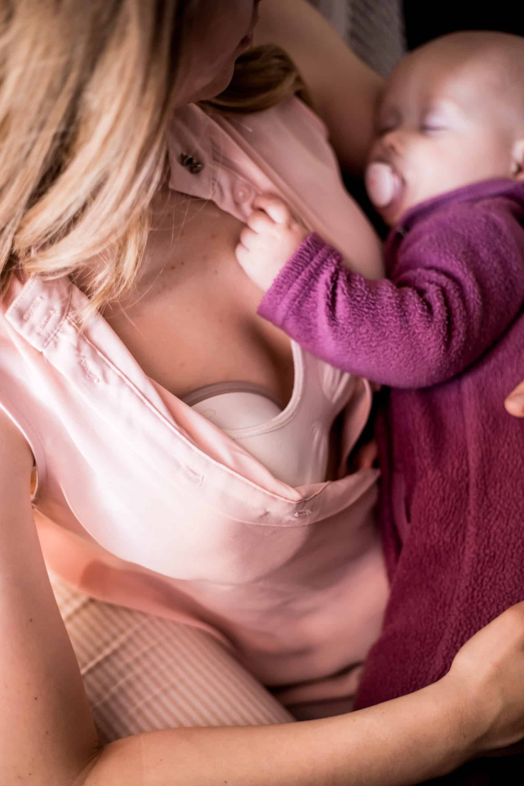 Mother holding baby while expressing milk with wearable breast pump